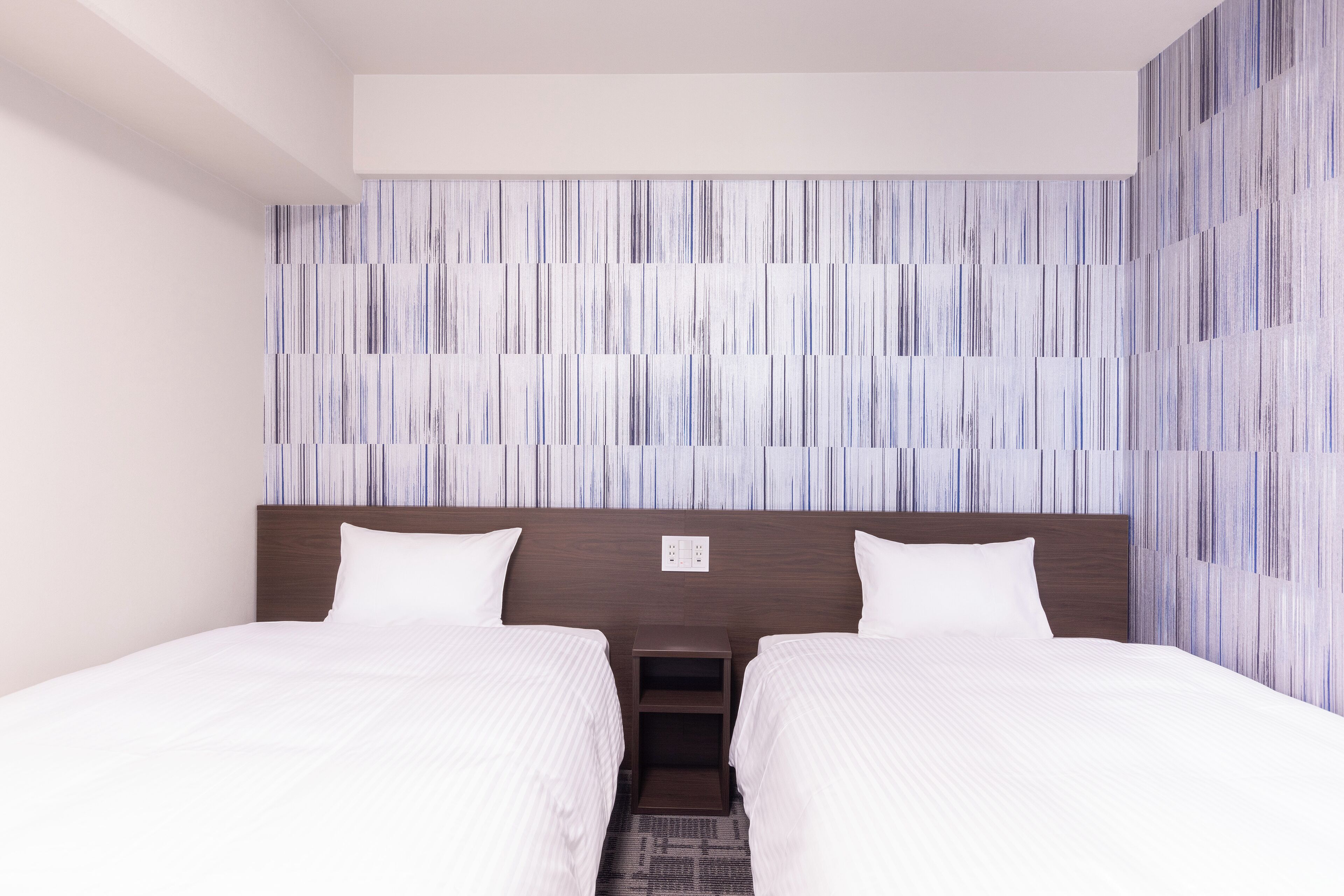 A hotel room with two beds, a wooden headboard, and a striped wall design.