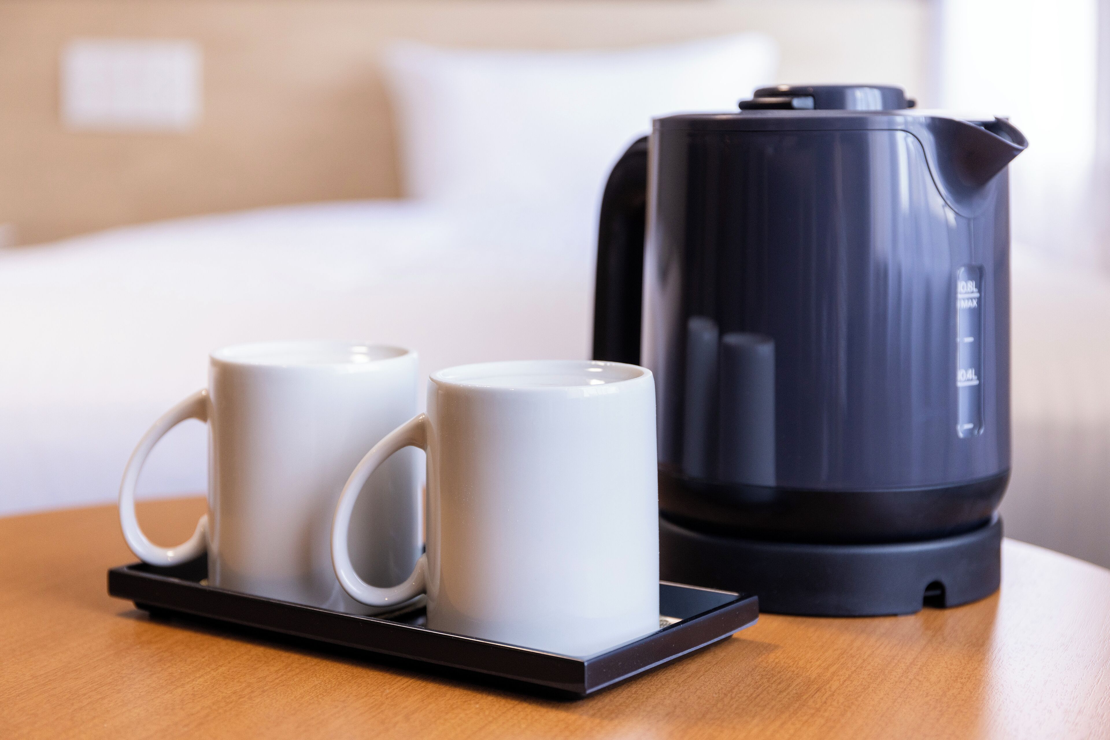 Una tetera eléctrica negra y dos tazas blancas sobre una bandeja.