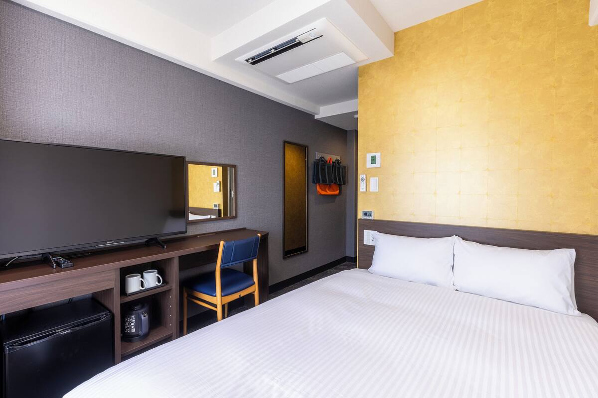 A hotel room with a bed, a desk with a chair, a coffee maker, and a television.