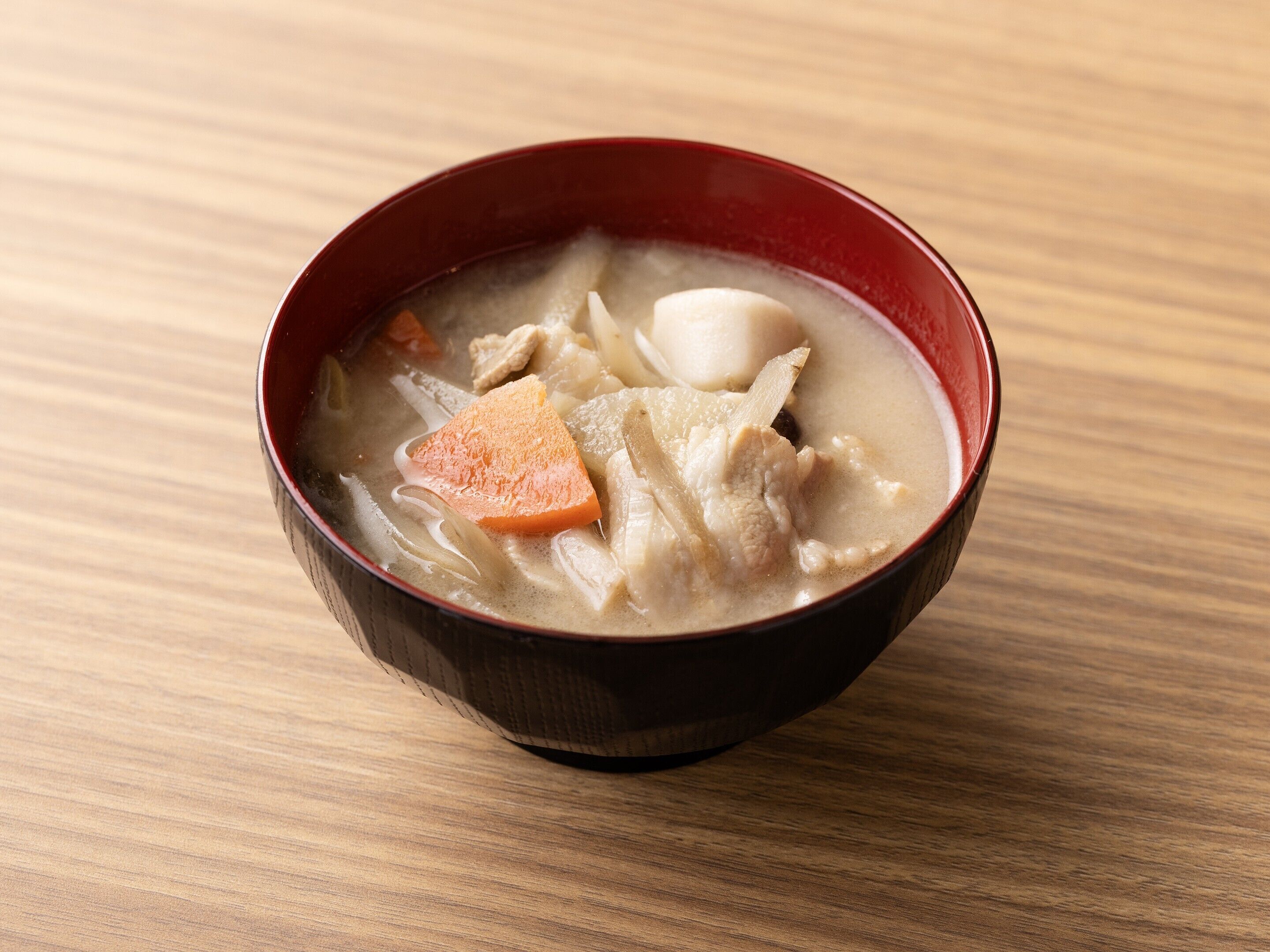 A bowl of soup with various ingredients on a wooden surface.
