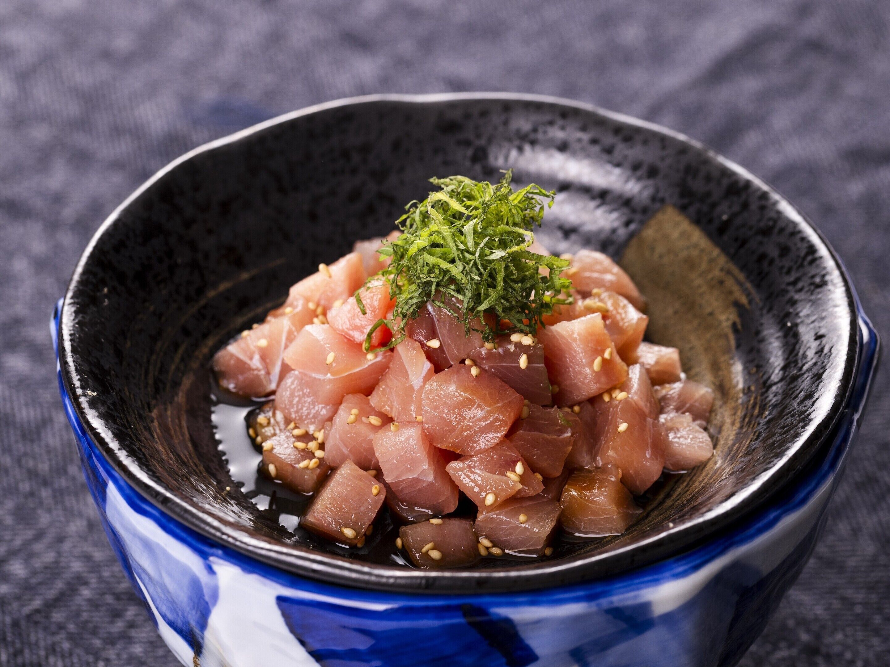 A bowl of sashimi with sesame seeds and green garnish.