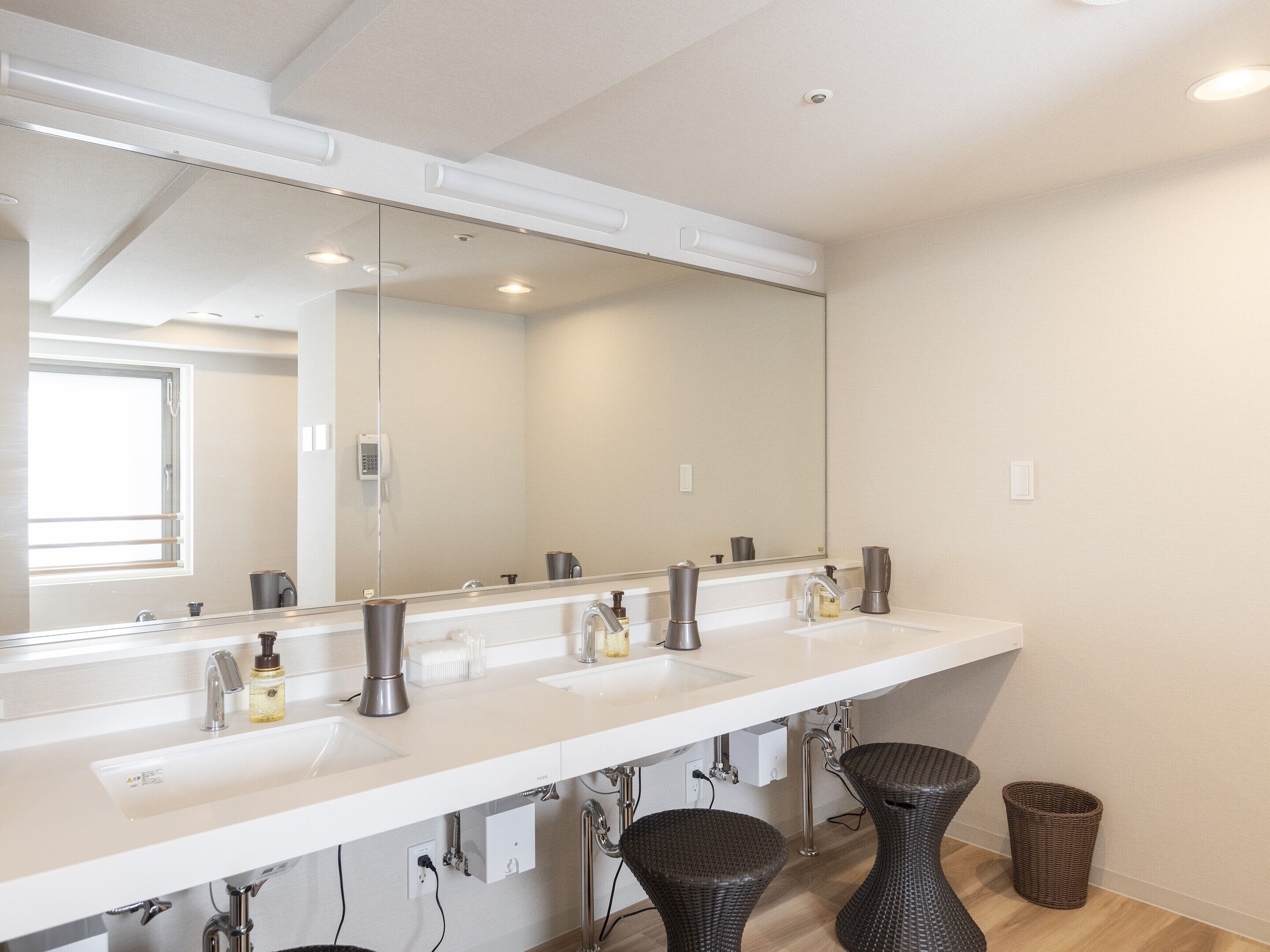 A modern bathroom with a large mirror, two sinks, and a trash bin.