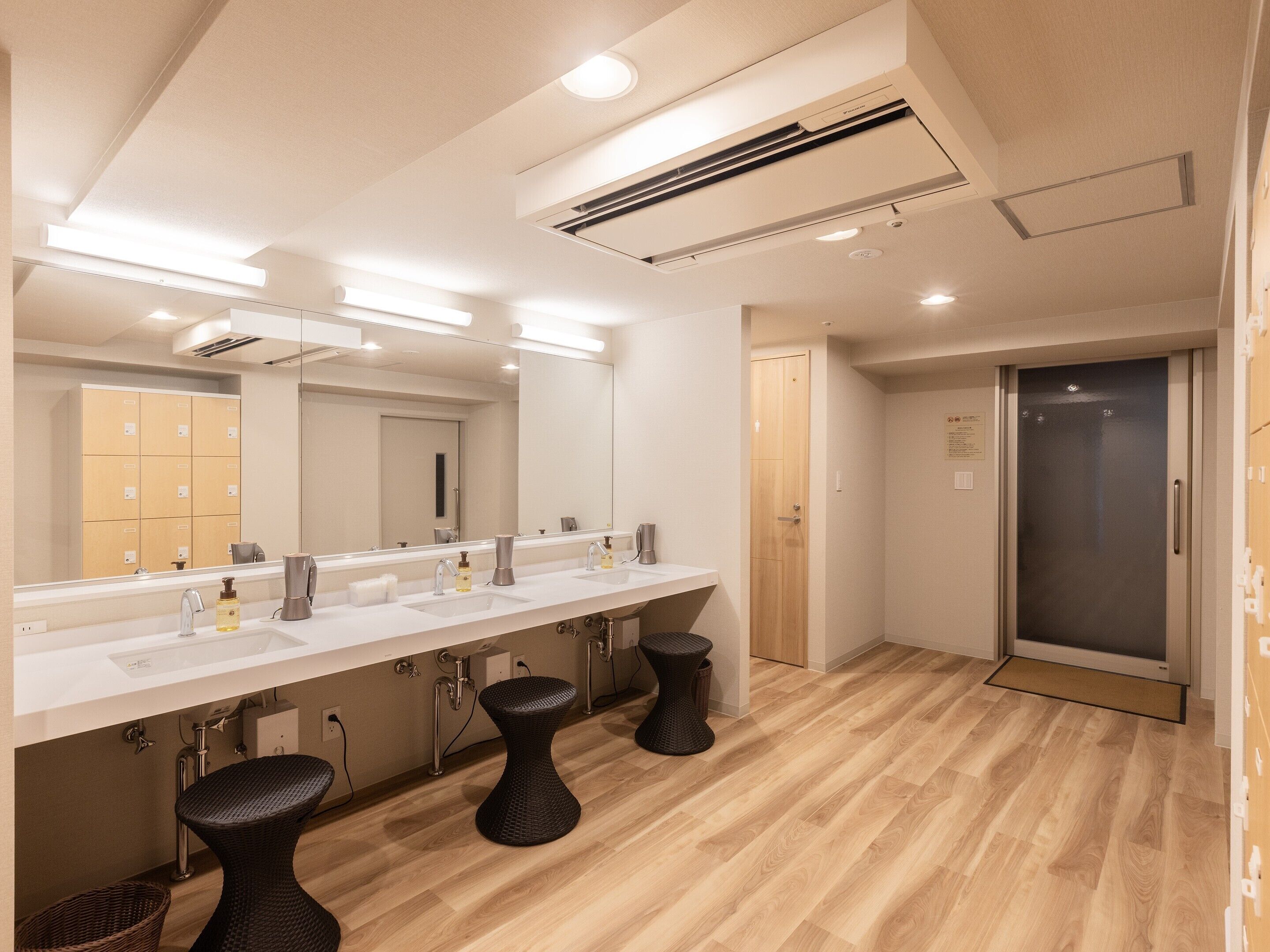 Une salle de bain moderne avec un long meuble-lavabo, trois tabourets noirs et un grand miroir.