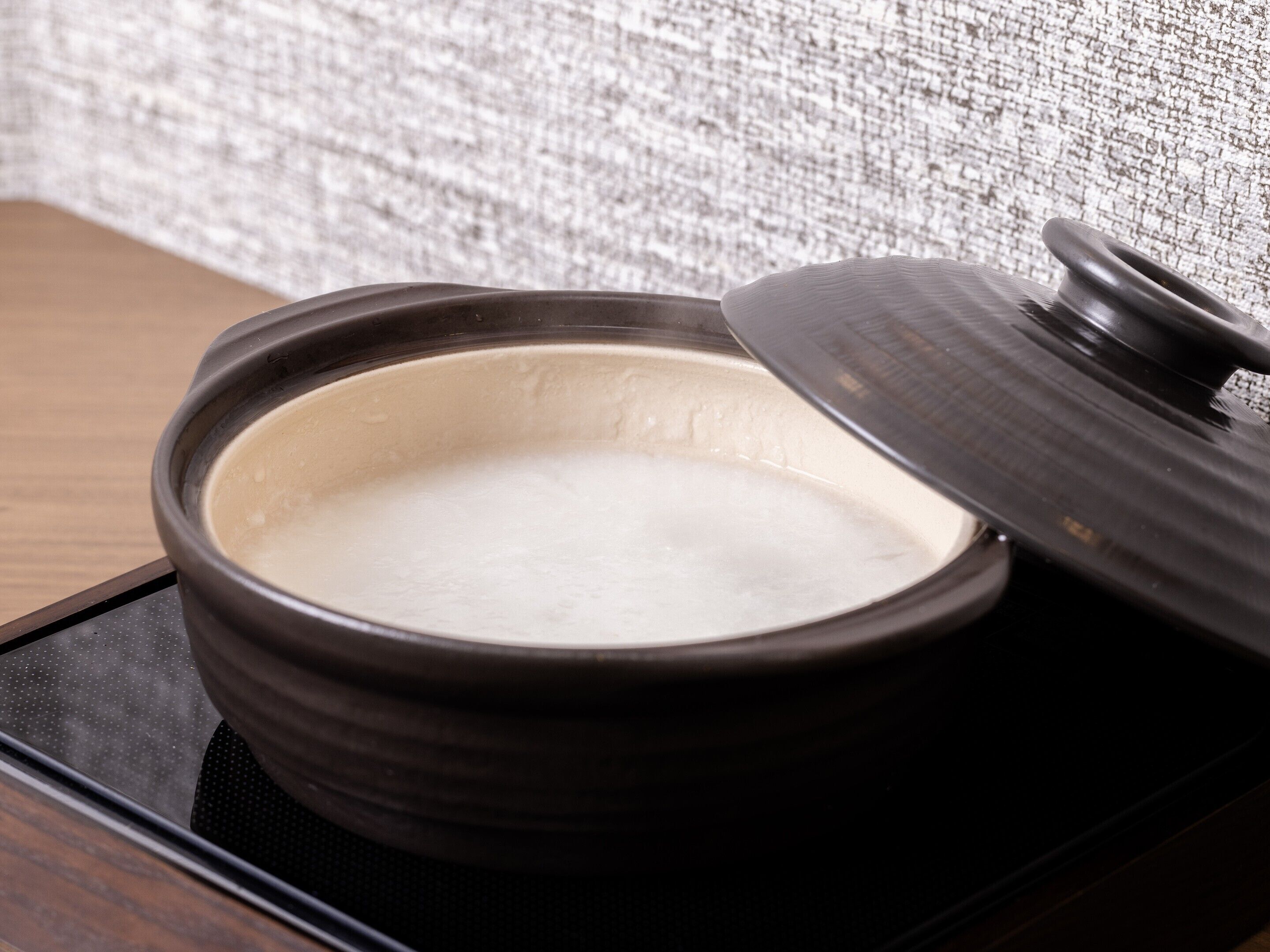 A dark ceramic bowl with a lid on a black tray.