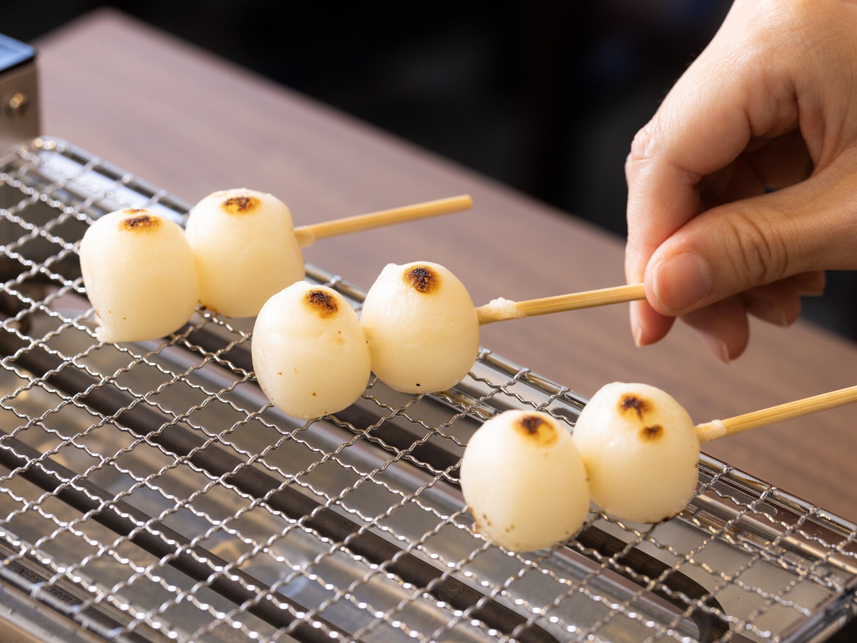 A person grilling mochi on a wire rack.