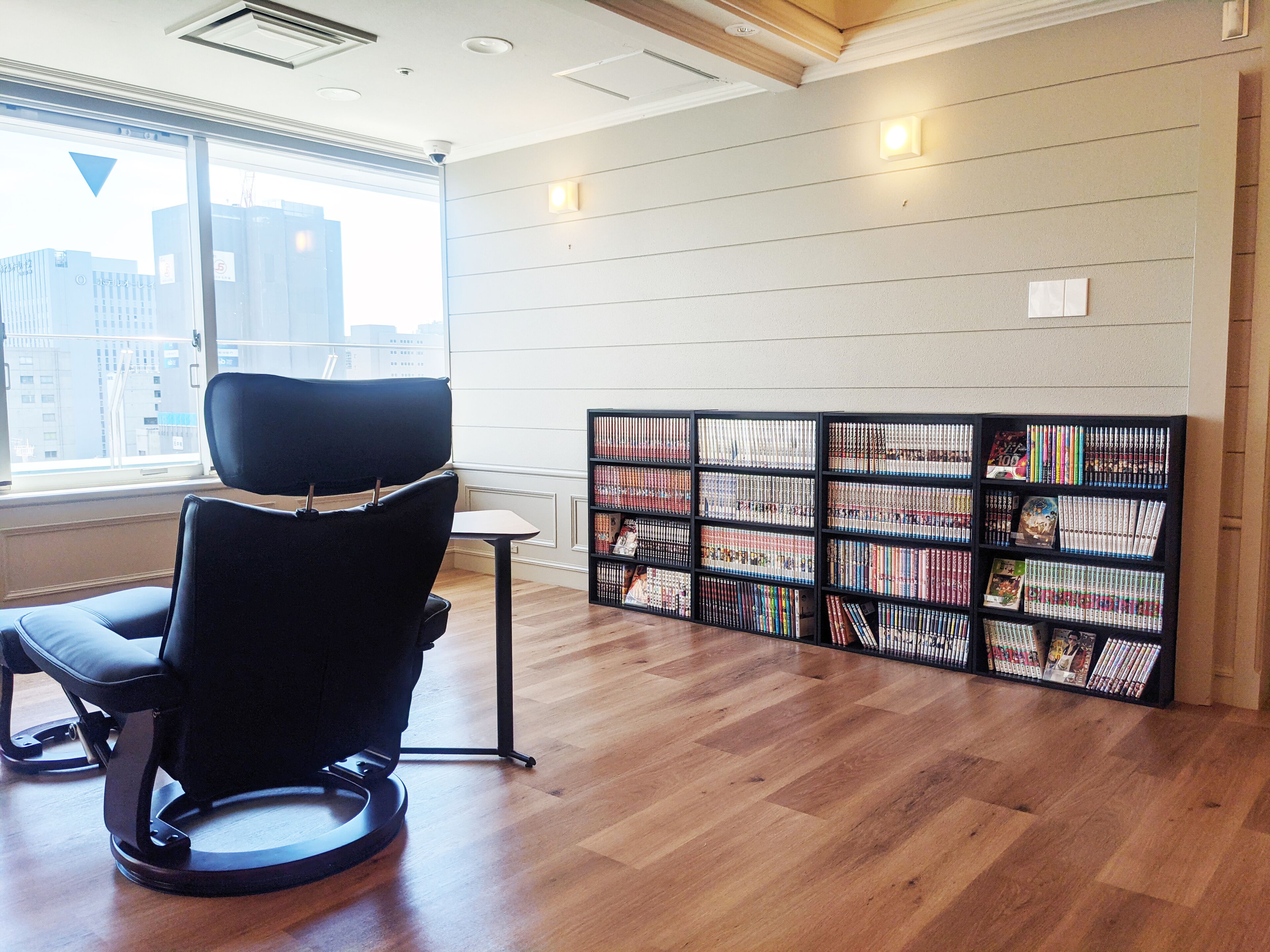 A library with a black chair, wooden flooring, and bookshelves.