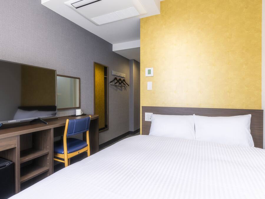 A hotel room with a bed, a desk with a chair, a television, and a coat rack.