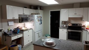 Una cocina con armarios blancos, microondas, refrigerador con imanes, estufa y una encimera con un pastel.