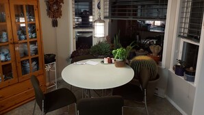 Un comedor con una mesa redonda, cuatro sillas, un armario de madera con puertas de vidrio y varias plantas en macetas.
