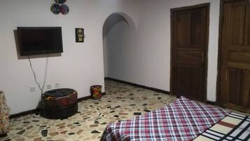 Una habitación con cama, televisor montado en la pared, una puerta y piso de baldosas.