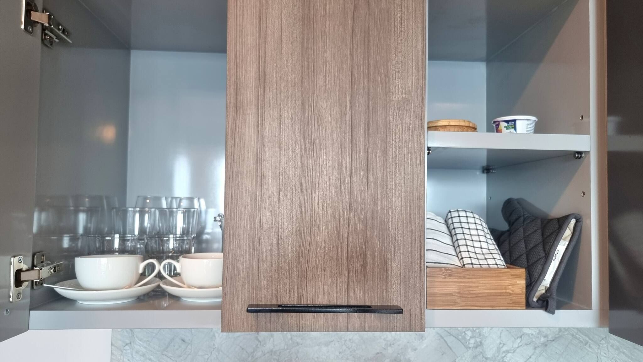 A modern kitchen with a wooden cabinet, a built-in sink, and a countertop with glassware and a kettle.