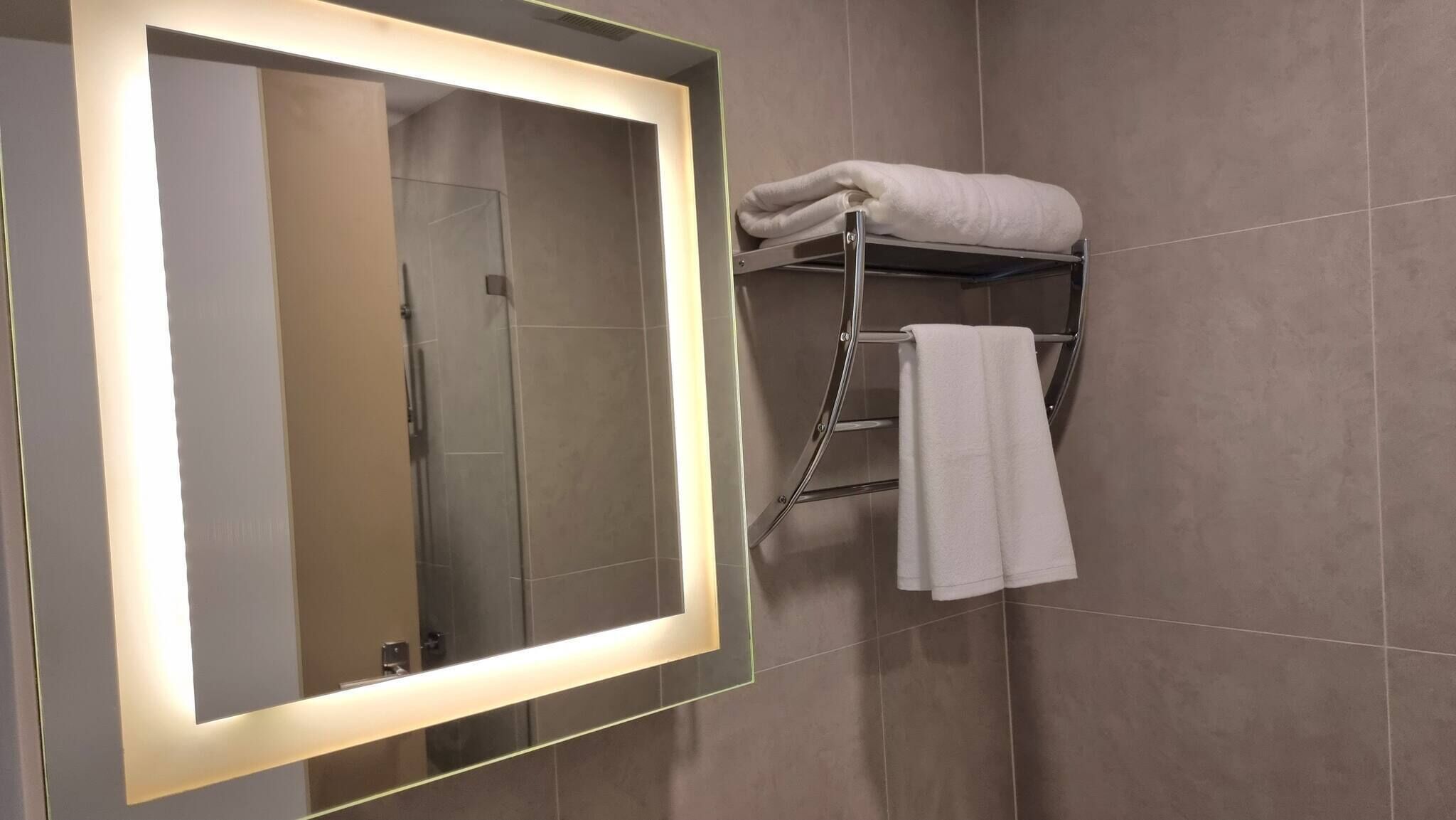 Un baño con un espejo grande, un perchero y una zona de ducha.