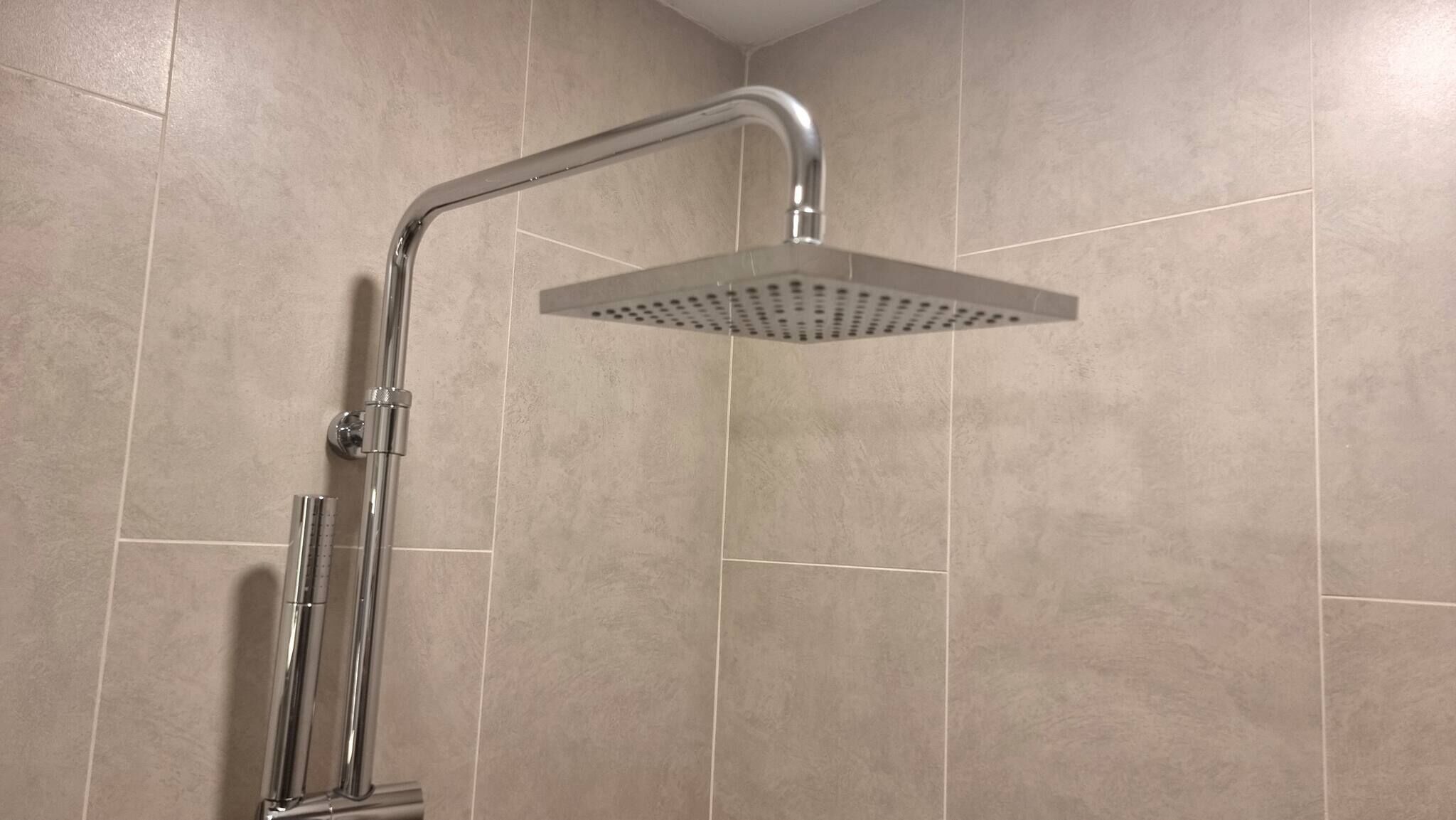 Eine Dusche mit chromfarbenem Wasserhahn und einer quadratischen Brause am Wand montiert.