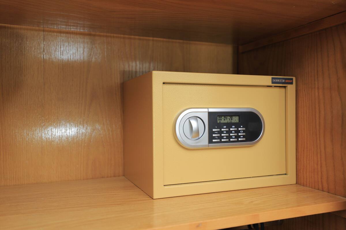 A beige safe with a digital keypad, placed on a wooden shelf in a wooden cabinet.