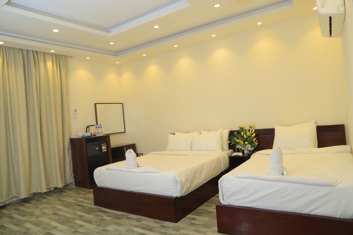 A hotel room with two beds, a desk, a mirror, and a nightstand with a vase of flowers.