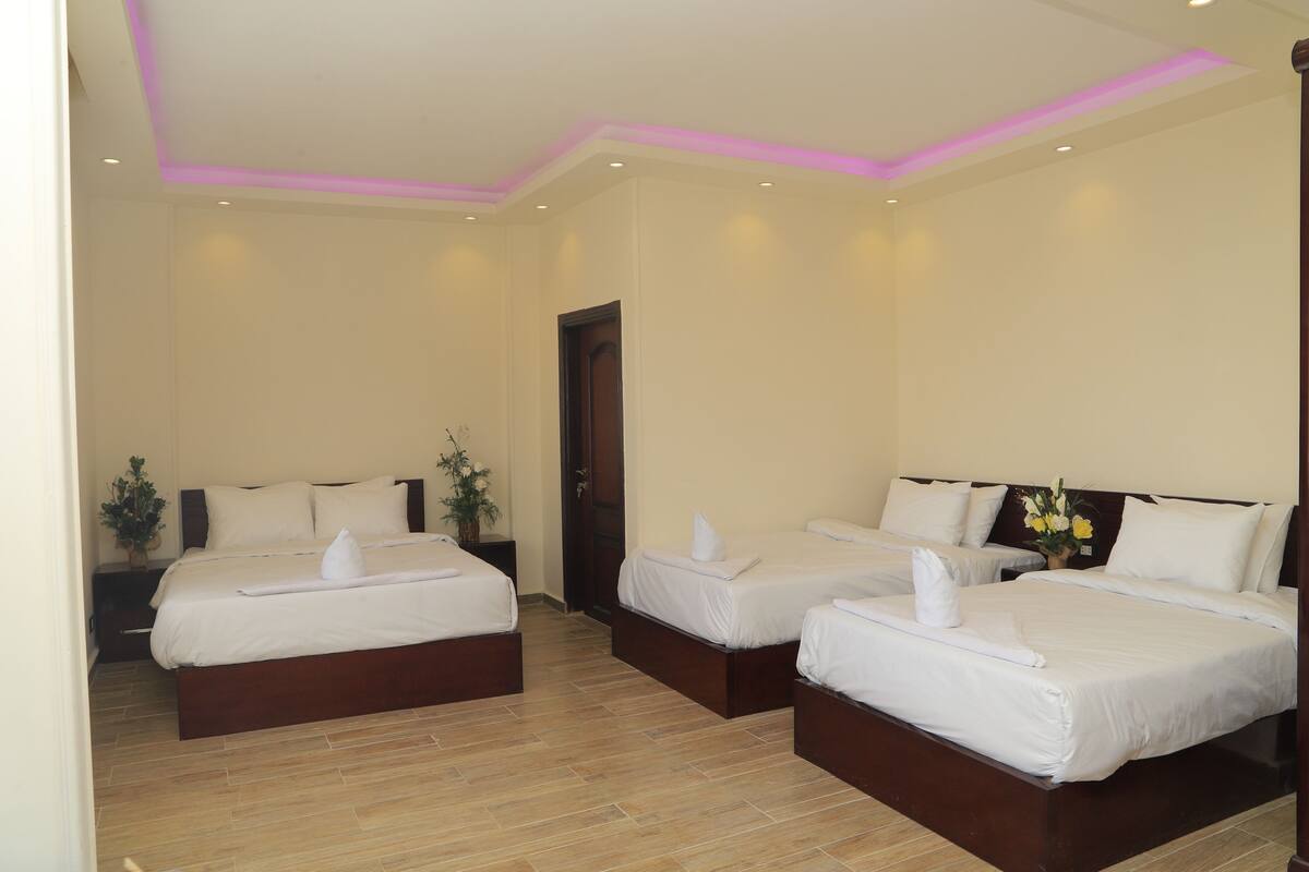 A hotel room with three beds, a wooden floor, and a door.
