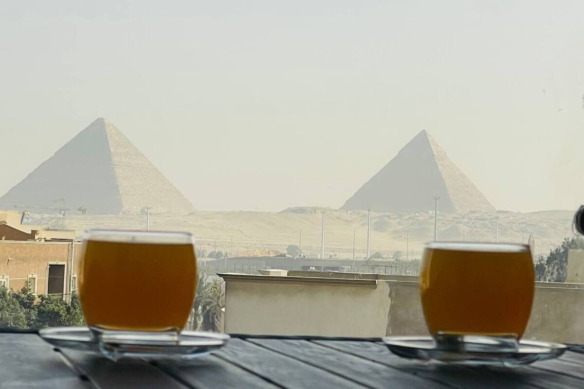 Two glasses of amber liquid on a wooden table with a view of two pyramids in the background.