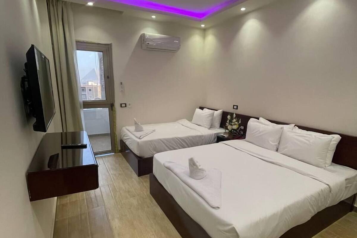 A hotel room with two beds, a flat-screen TV, an air conditioning unit, and a view of the outside.