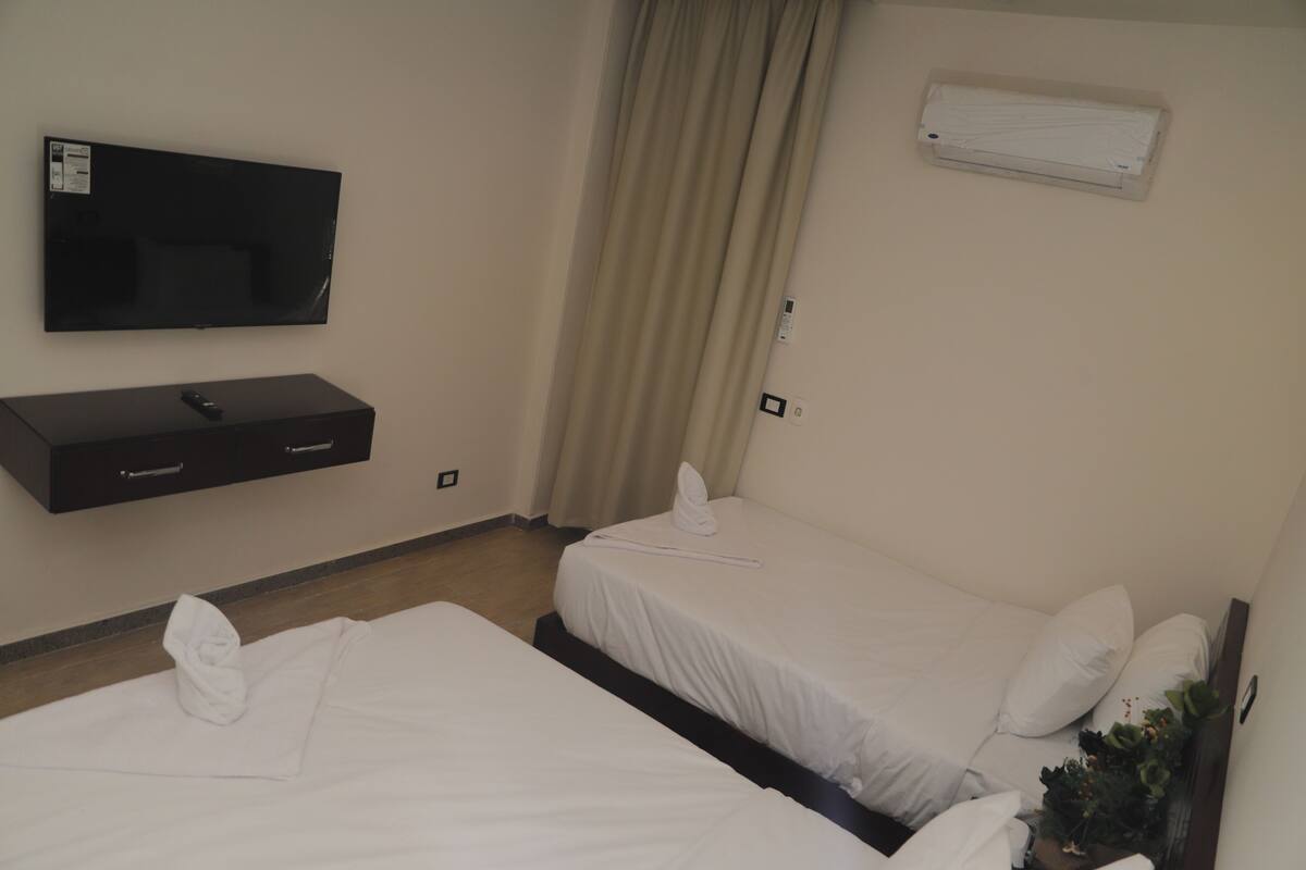 A hotel room with two beds, a TV, and a wall-mounted air conditioner.