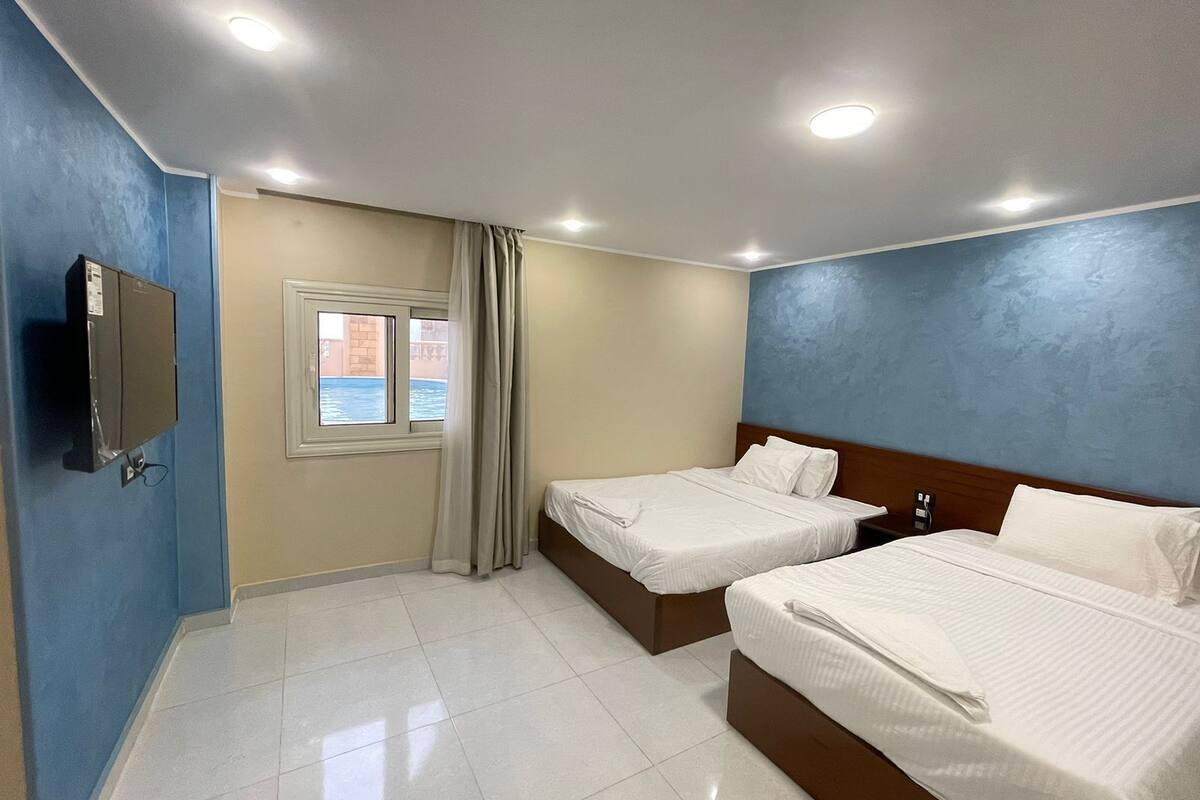 A hotel room with two beds, a TV, a window with curtains, and a view of the outside.
