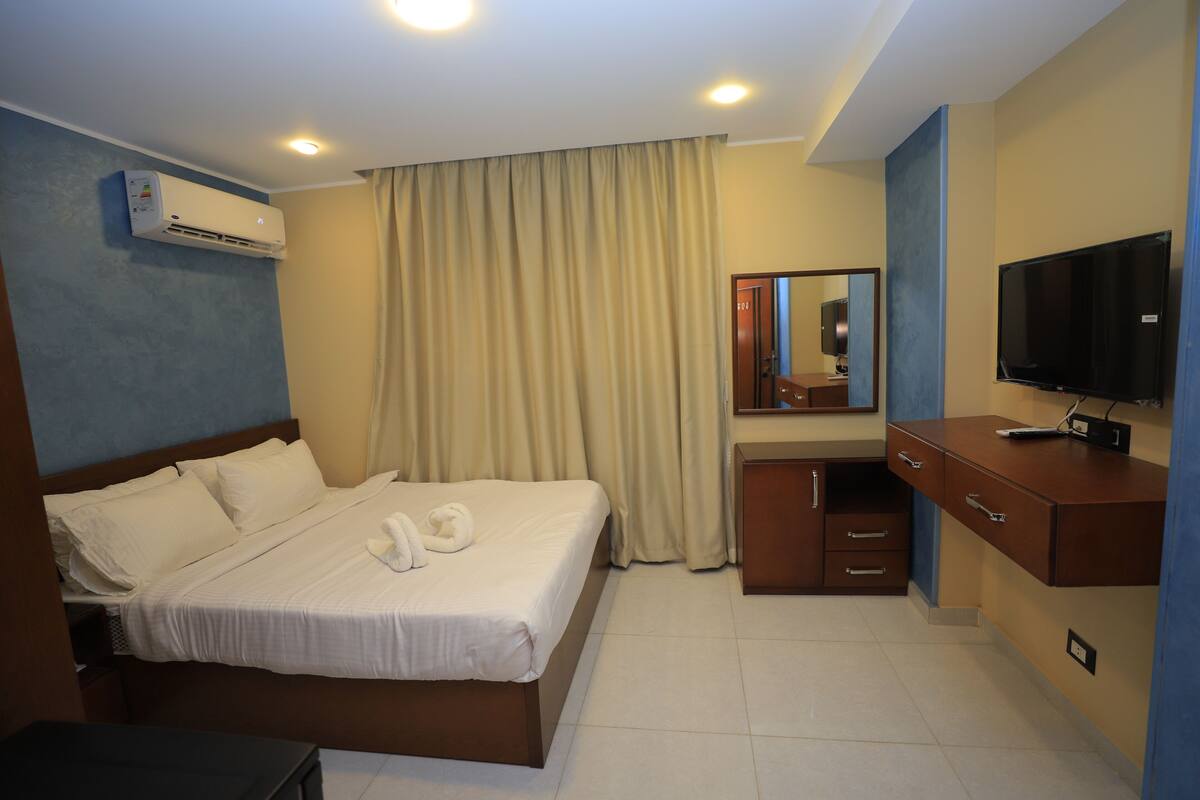 A hotel room with a bed, a desk, a television, and an air conditioning unit.