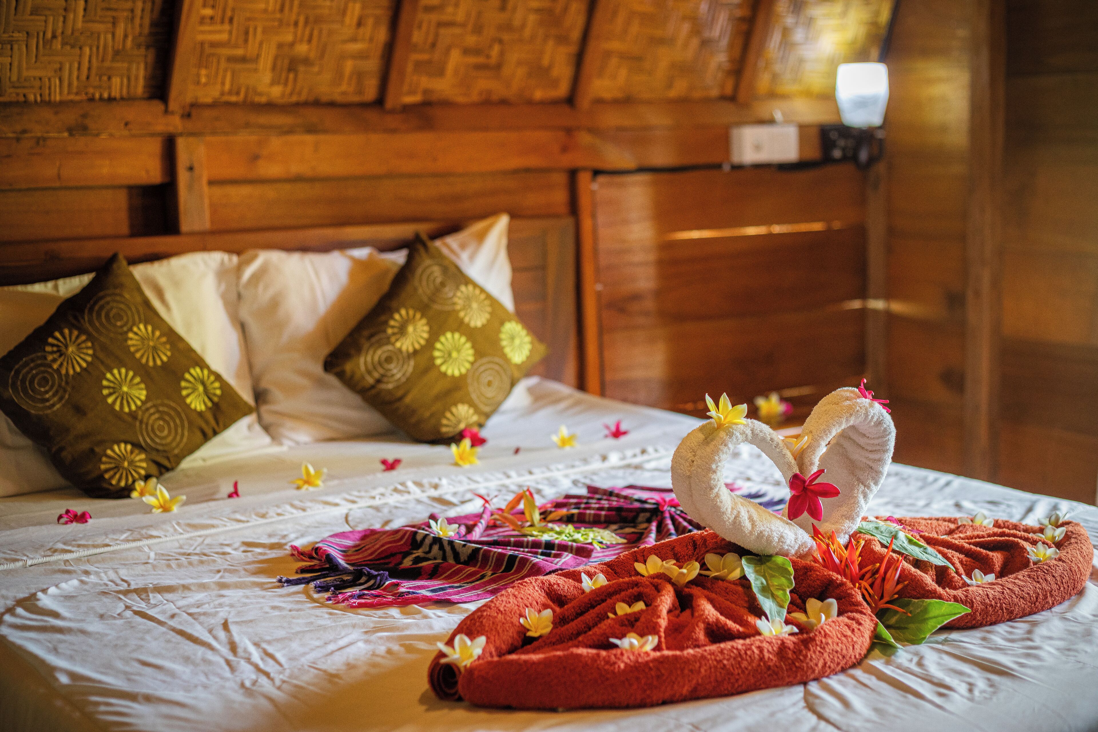 Ein Bett mit weißer Bettdecke, zwei Kissen mit Blumenmuster und ein rotes Handtuch mit Blumen sowie eine herzförmige Handtuchgestaltung.