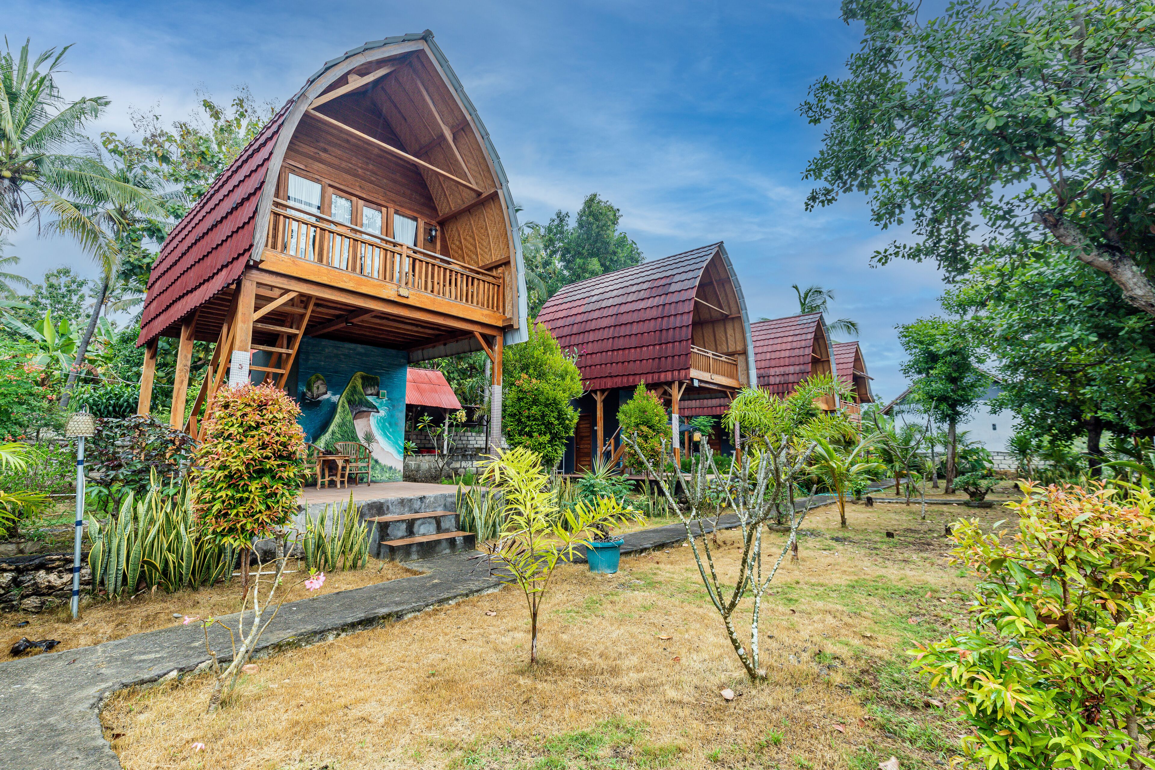 A wooden house with a balcony, surrounded by tropical vegetation.