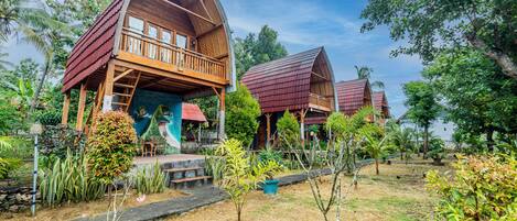 A wooden house with a balcony, surrounded by tropical vegetation.