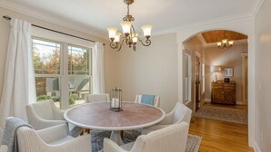 Ein Esszimmer mit einem runden Tisch, weißen Polsterstühlen, einer Kandelaber und Blick durch große Fenster.