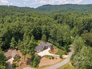 A two-story house surrounded by dense forest, with a driveway leading to the front entrance. - One Story Luxury near Hendersonville & the Biltmore! (Hendersonville)