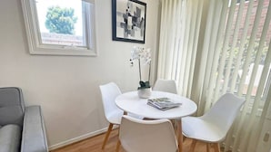 Un comedor con una mesa redonda, cuatro sillas, una planta en maceta y un cuadro en la pared.