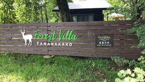 A wooden fence with a deer silhouette and the text "Forest Villa Yamanakako" and "Forest Kitchen Garden Living" with operating hours. - Forest Villa Yamanakako (Yamanakako)