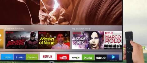 A television screen displaying a Netflix interface with various shows and a remote control in hand.