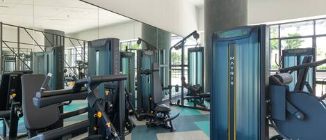 A modern gym with various exercise machines, large windows, and a clean, spacious layout.