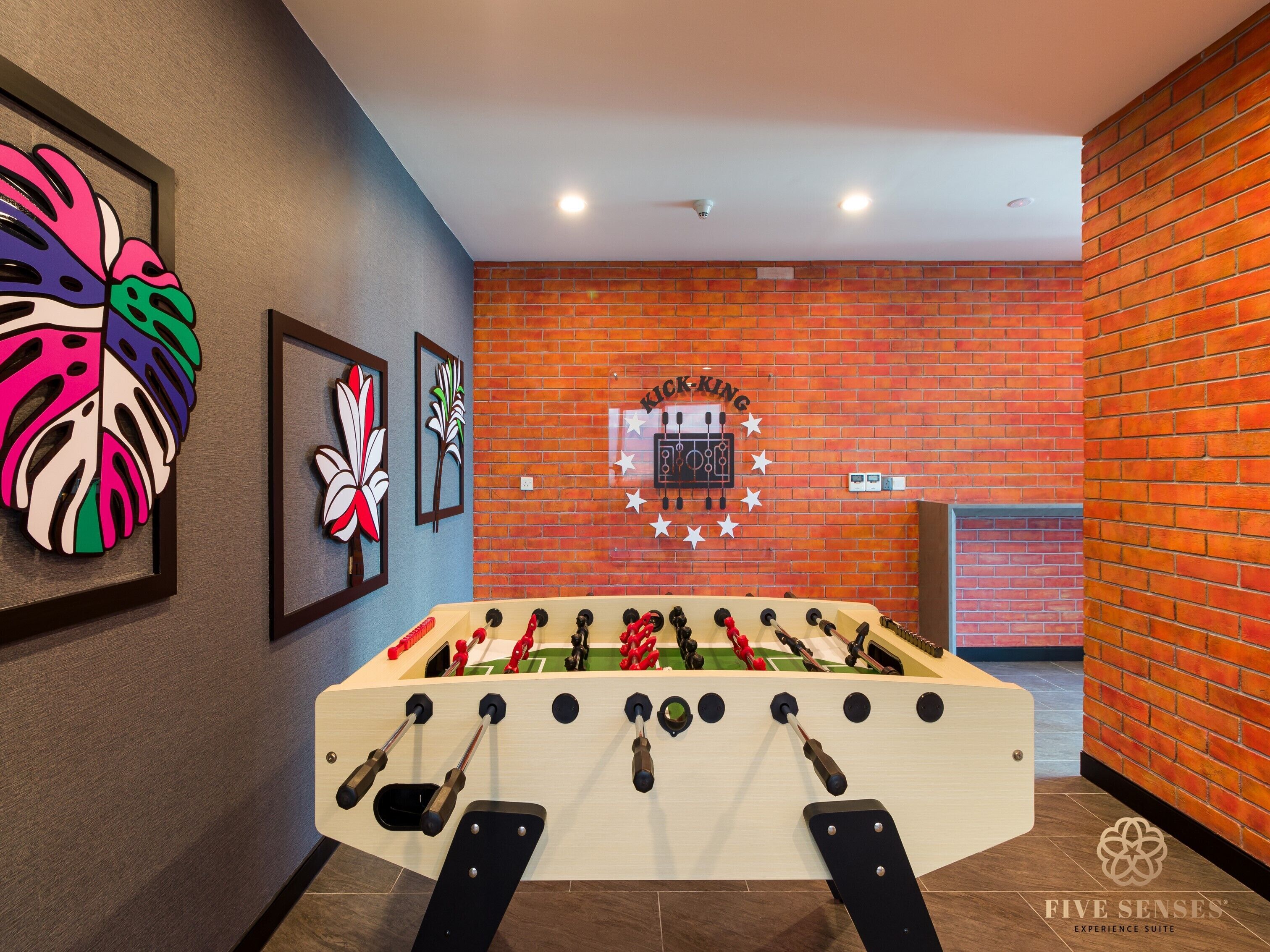 Una mesa de fútbol de mesa en una habitación con pared de ladrillo y obras de arte enmarcadas.