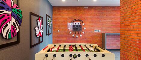 Una mesa de fútbol de mesa en una habitación con pared de ladrillo y obras de arte enmarcadas.