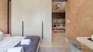 Quarto de hotel moderno com cama, escrivaninha e cozinha compacta.