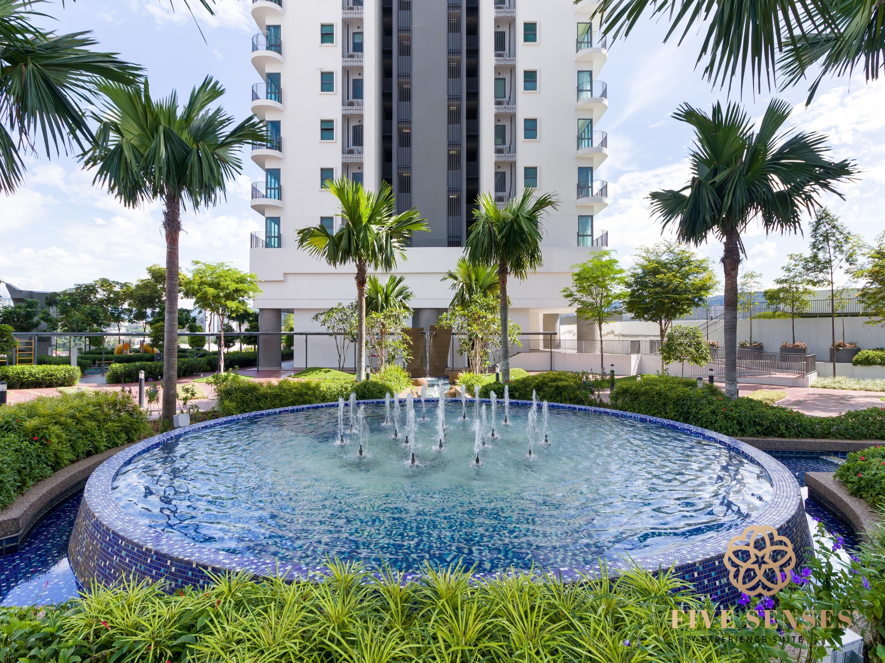 A modern hotel with a central circular pool surrounded by lush greenery and palm trees.