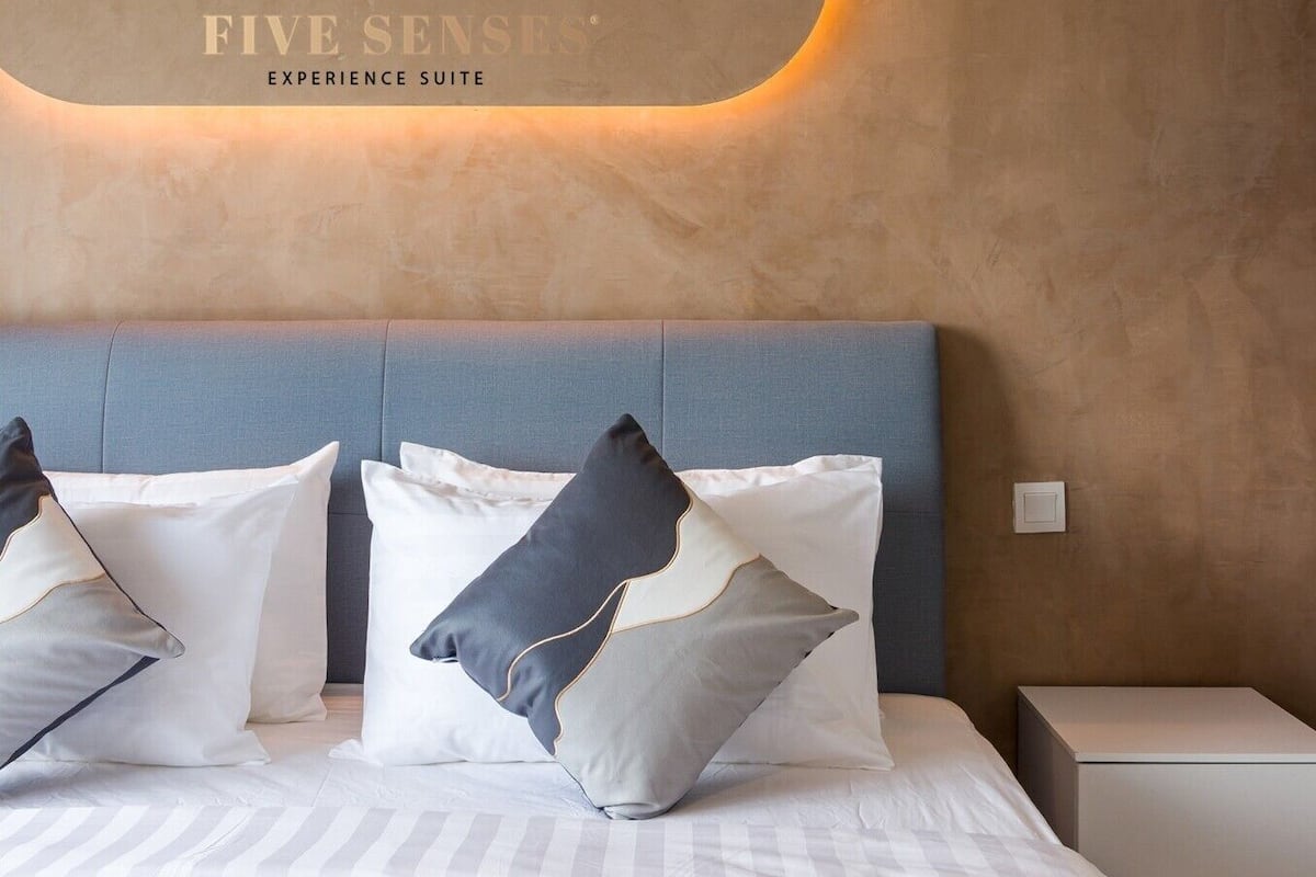 A hotel room with a bed, pillows, a nightstand, and a wall-mounted sign.