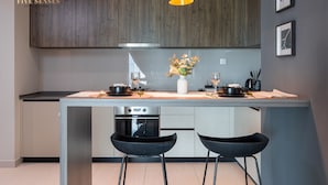 Uma cozinha moderna com armários de madeira escura, uma ilha central com banquetas, uma luminária pendente e um vaso com flores.