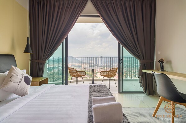Habitación de hotel con cama, escritorio, dos sillas, balcón con mesa y sillas, y vistas a la ciudad.