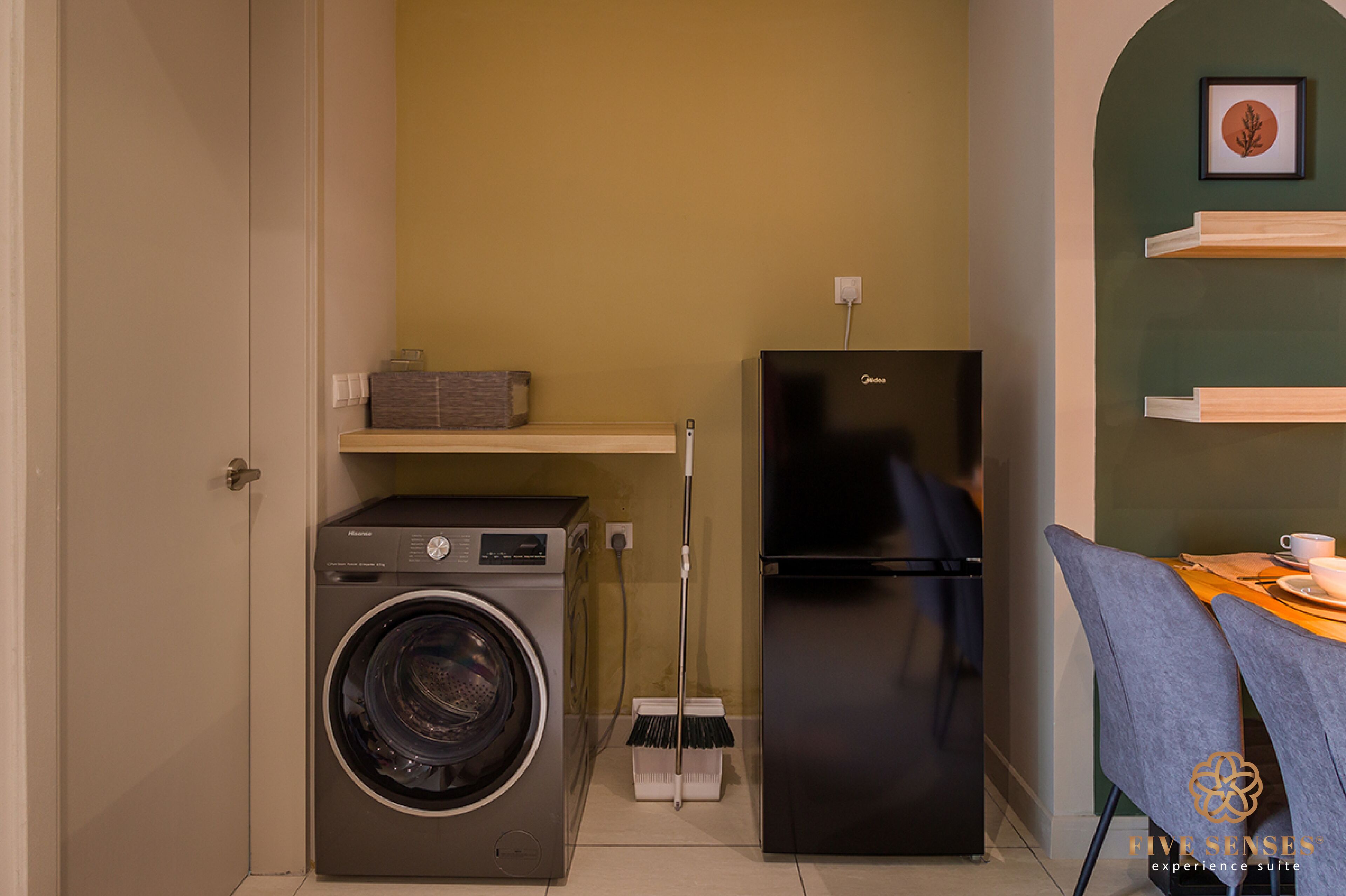 Une cuisine compacte équipée d’un lave-linge, d’un réfrigérateur, d’un balai, et d’un coin repas avec des chaises et une table.