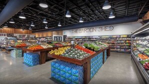 L’intérieur d’une épicerie, avec des présentoirs de fruits et légumes, des rayons réfrigérés et une enseigne indiquant « THE BARDON SHEED ».