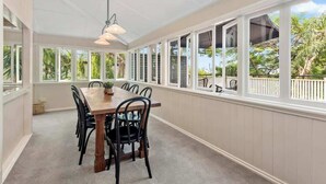 Un coin repas avec une table et des chaises en bois, de grandes fenêtres et un ventilateur de plafond.