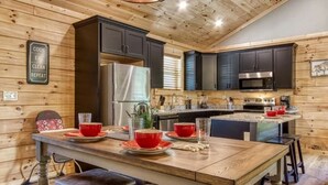 Une cuisine avec un lambris en bois, des meubles de couleur sombre, un réfrigérateur en acier inoxydable et un îlot central doté de tabourets.