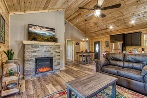 A cozy living room with a stone fireplace, a leather sofa, and a dining area with a table and chairs. - Brand New - King Bed Game Room & Hot Tub (Sevierville)