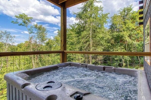 Relax in a hot tub on a raised deck overlooking a dense forest.