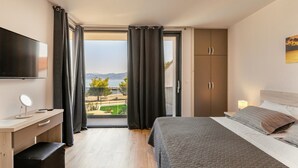 Ein Schlafzimmer mit Bett, Schreibtisch, Fernseher und Blick auf Strand und Berge.