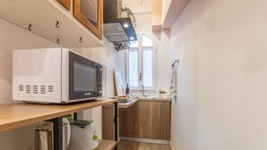 Een kleine keuken met een magnetron, een spoelbak en houten keukenkastjes.