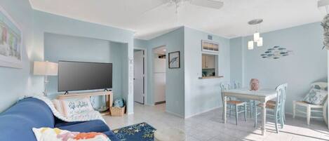 A living room with a blue sofa, a flat-screen TV, and a ceiling fan.
